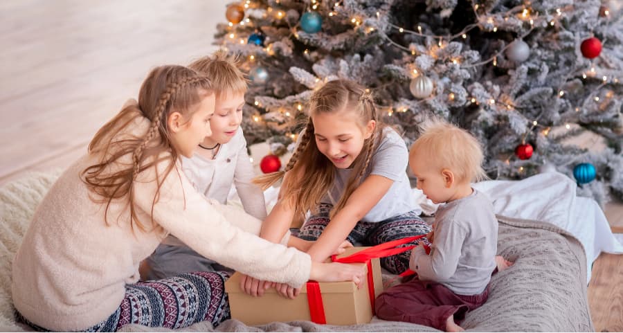 Children opening a present in the living room beside a Christmas tree.